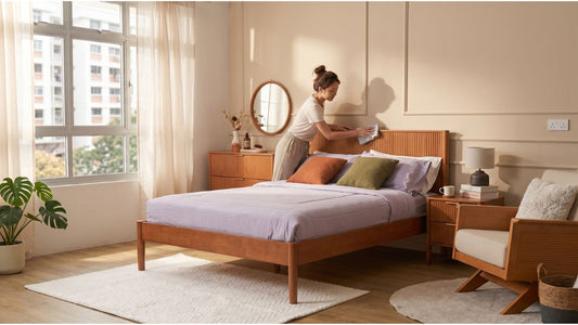 Woman cleaning a cherry wood bed frame in a warm Singapore bedroom with matching bedside tables and soft natural light