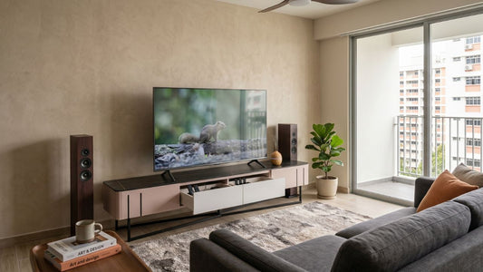 Modern TV console collection in a Singapore living room with wide storage cabinet, large TV, speakers, sofa, coffee table, and warm neutral styling.